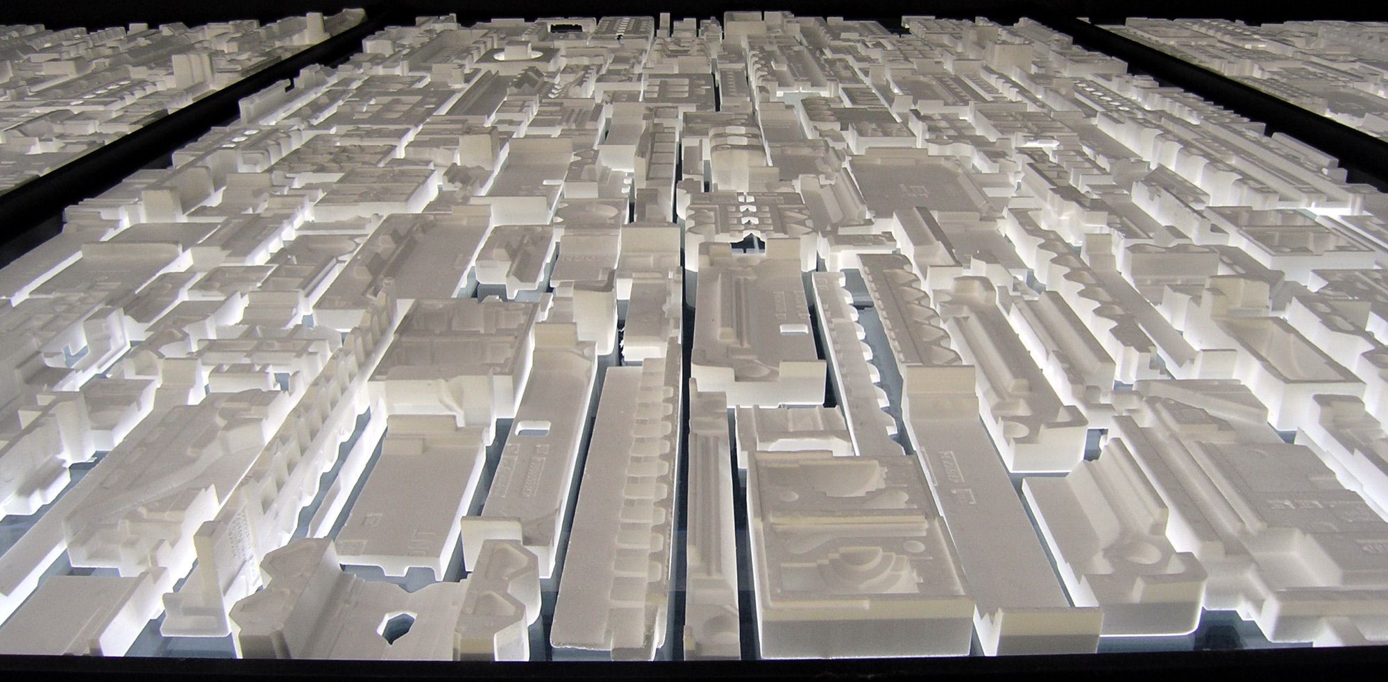 Detalle de una maqueta volumétrica blanca de una ciudad, retroiluminada, con manzanas y calles a escala