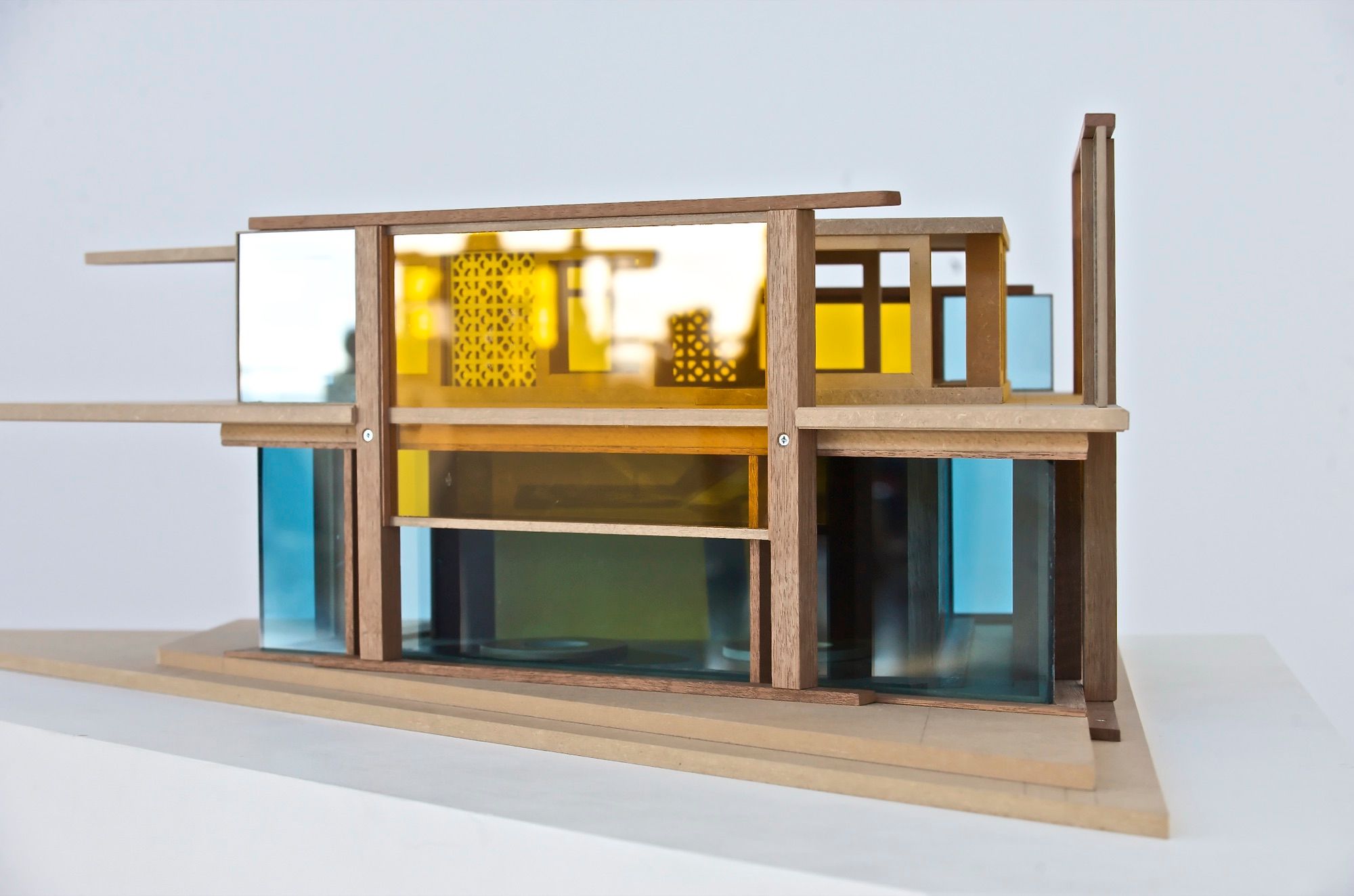 Maqueta de arquitectura de una vivienda con estructura de madera y paneles de metacrilato de color sobre fondo blanco
